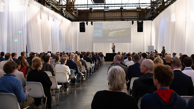 Op het podium van het Waterinnovatiefestival Martijn Bouman en daarvoor een volle zaal met publiek